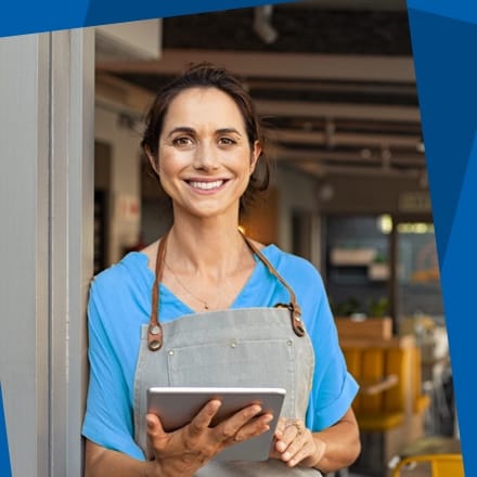A woman business owner in an apron holding a tablet.