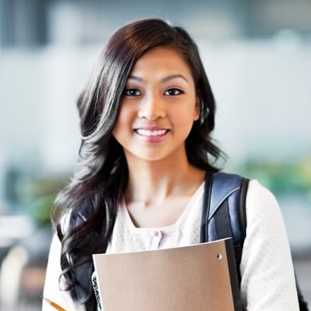 A young woman student with a bookbag carrying a notebook.