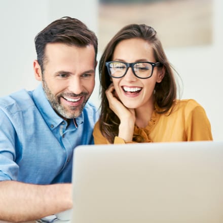 A young couple smiling while looking at a laptop.