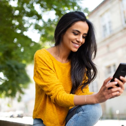 A young woman smiling while using a smartphone.