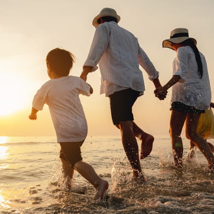 A family holding hands and running towards the beach.