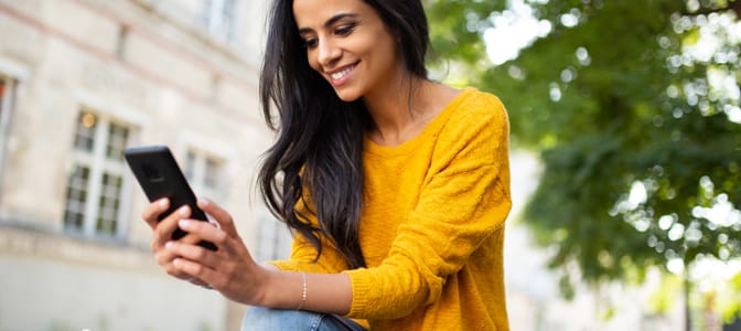 A smiling young woman looking down at her mobile device.