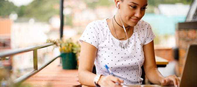 A high school student studying outdoors on a patio wearing ear buds.