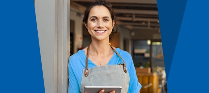 A woman business owner in an apron holding a tablet.