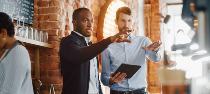 Two business professionals reviewing plans together inside a modern cafe setting.
