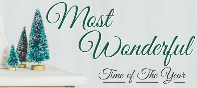 Small scale christmas trees and a cottage resting on a white table. To the right, the words: most wonderful time of the year.