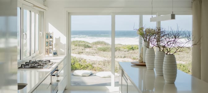 A view through a modern, white kitech into the ocean front backyard.