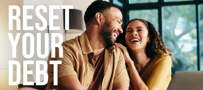 A couple smiling at each other sitting in front of a laptop. The words on the left: reset your debt.