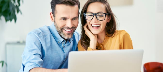 A young couple smiling while looking at a laptop.