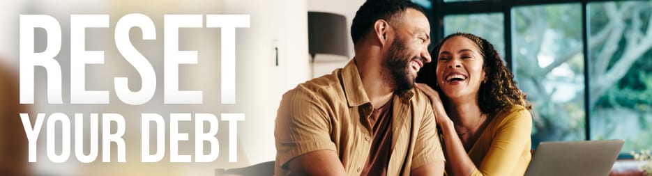 A couple smiling at each other sitting in front of a laptop. At the left, the words: reset your debt.