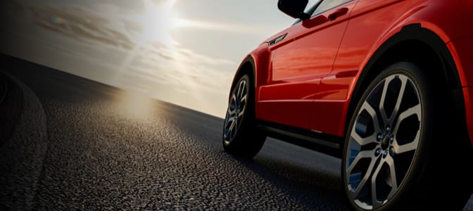 A side shot of a red car with the sun setting in the background.