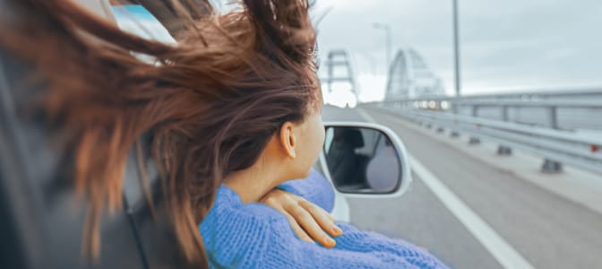 Four young people driving in a convertible with outstretched arms.