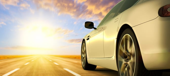A side view of a silver sports sedan driving on a long, empty, three-lane road.