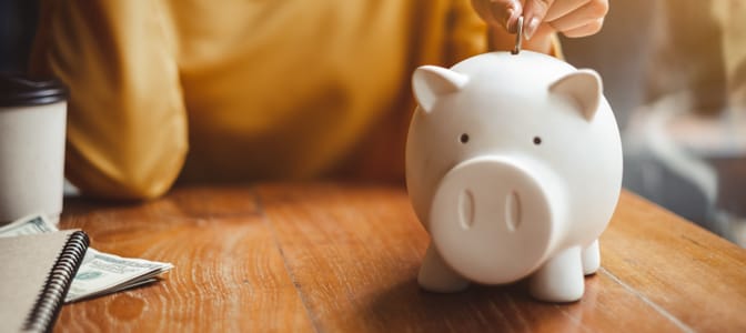 A hand dropping a coin into a piggy bank.
