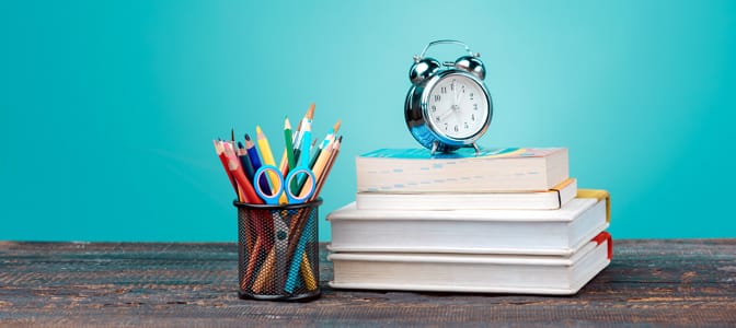 A silver alarm clock resting on a stack of books.