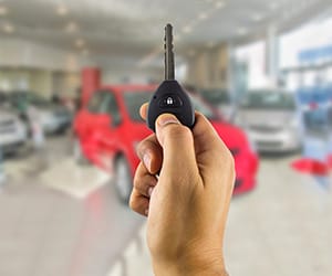 A hand holding an automobile key inside an auto delearship